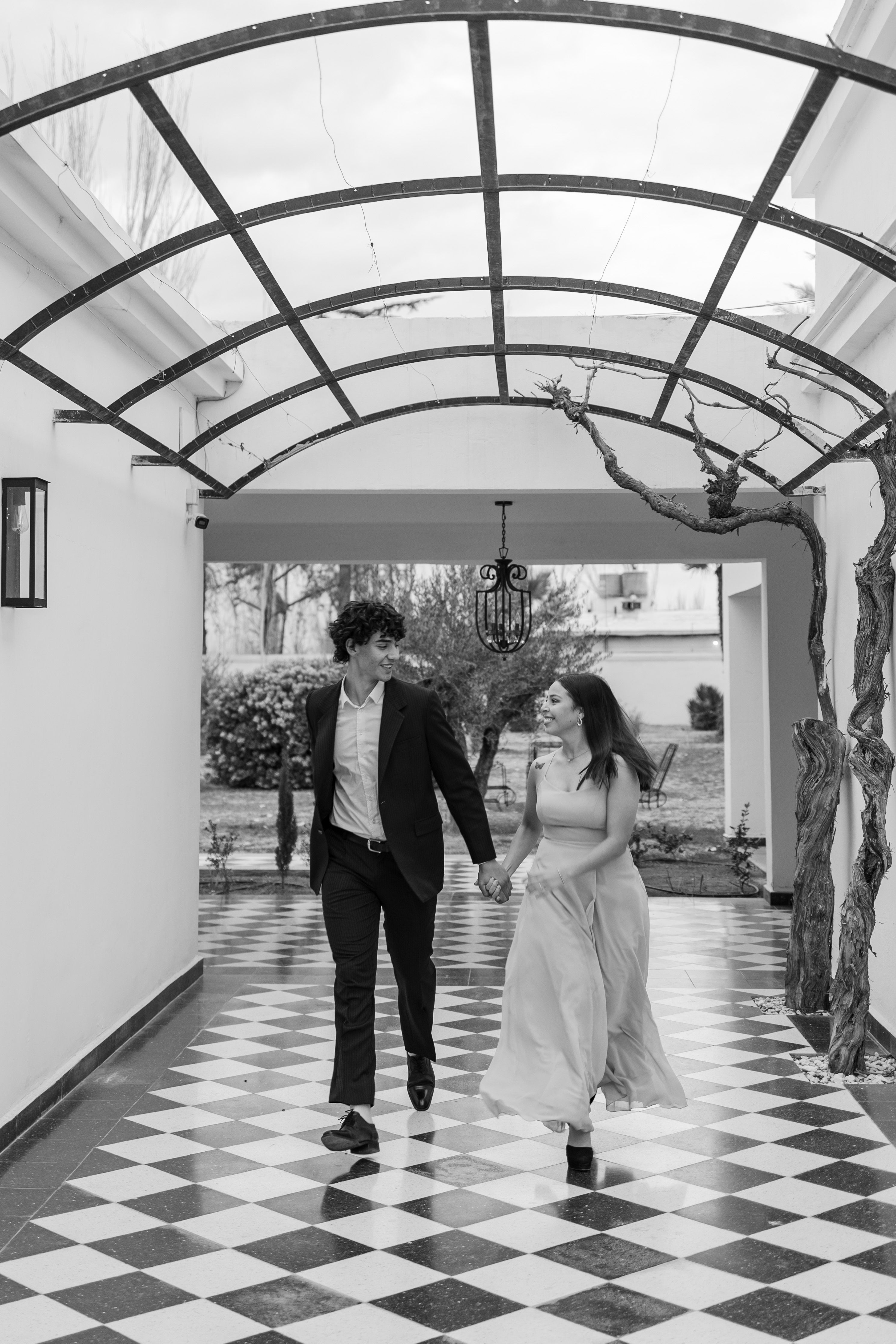 A couple holding hands walking under a pergola in Luján de Cuyo, Mendoza.