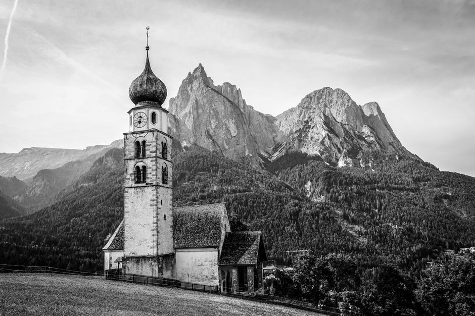 A black and white image of a church against a stunning mountain backdrop in South Tyrol.