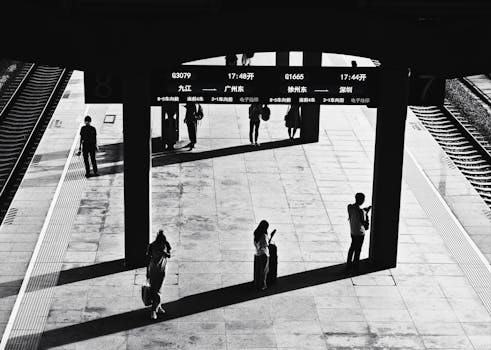 Monochrome image of a train station with people waiting, creating dramatic shadows.
