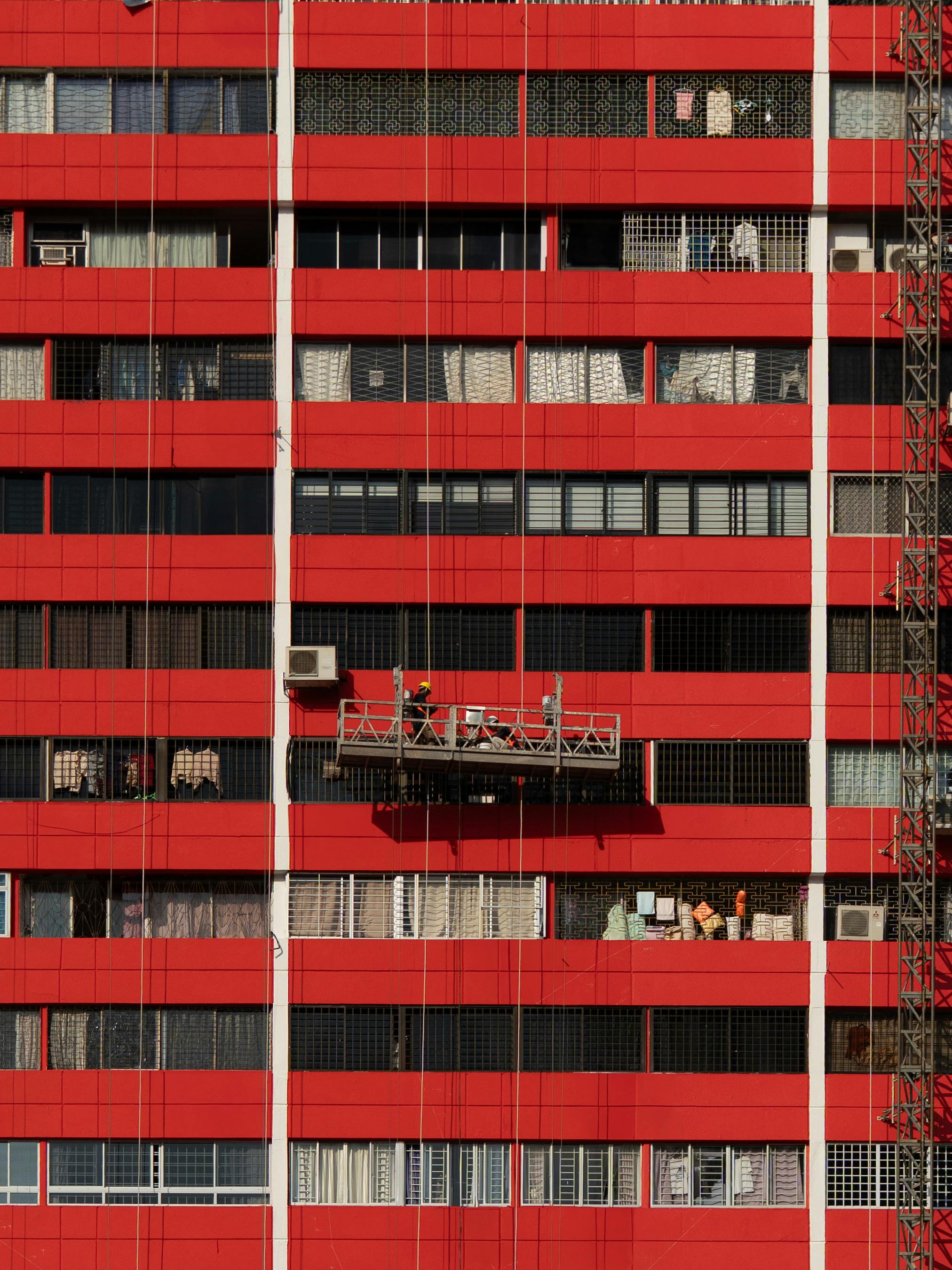 Bright red apartment building facade in Singapore's Chinatown with workers on suspended platform.