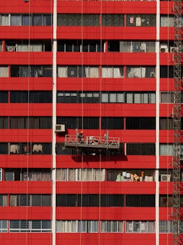 Bright red apartment building facade in Singapore's Chinatown with workers on suspended platform.