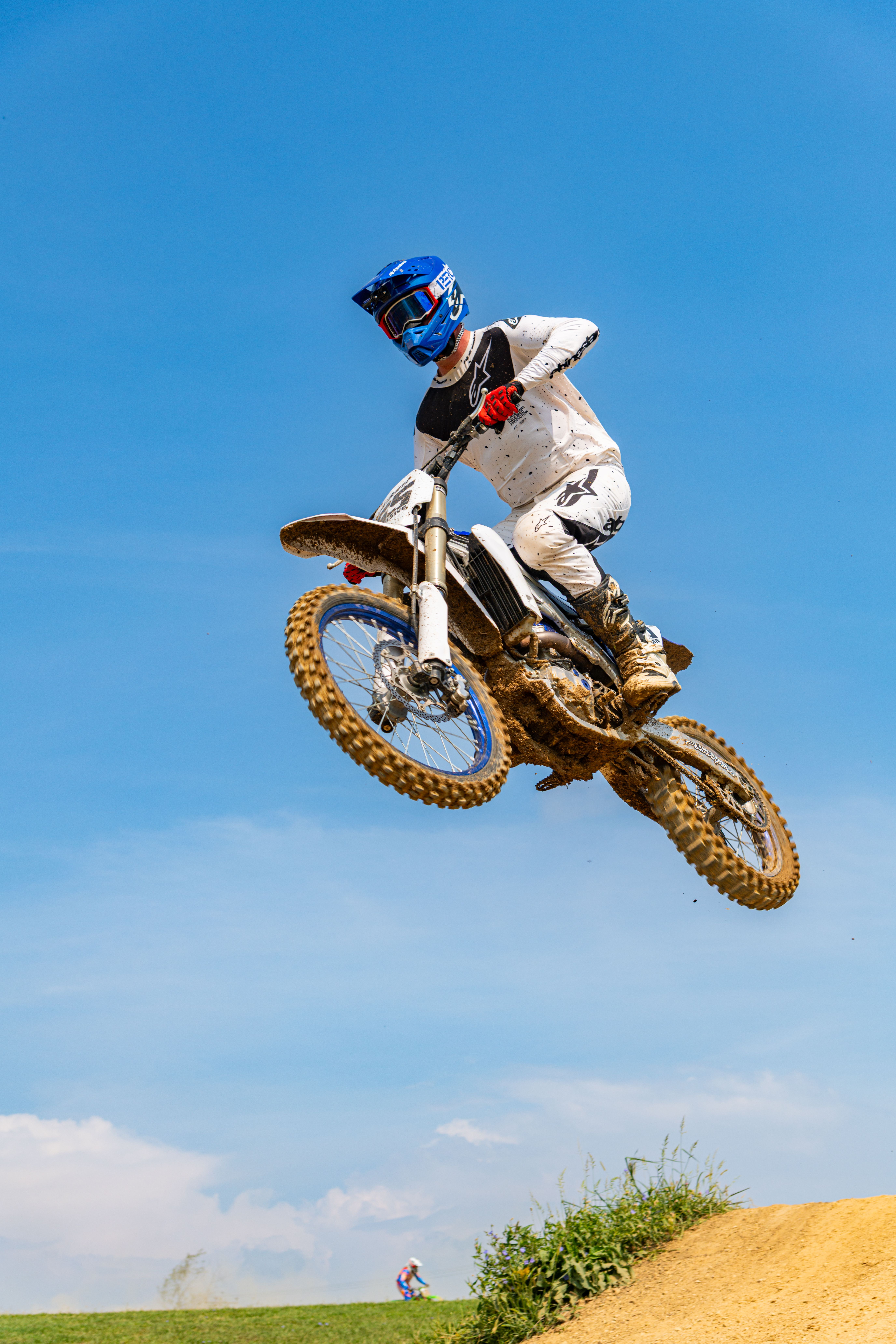 A motorcyclist performs a jump on a dirt track under clear blue skies.