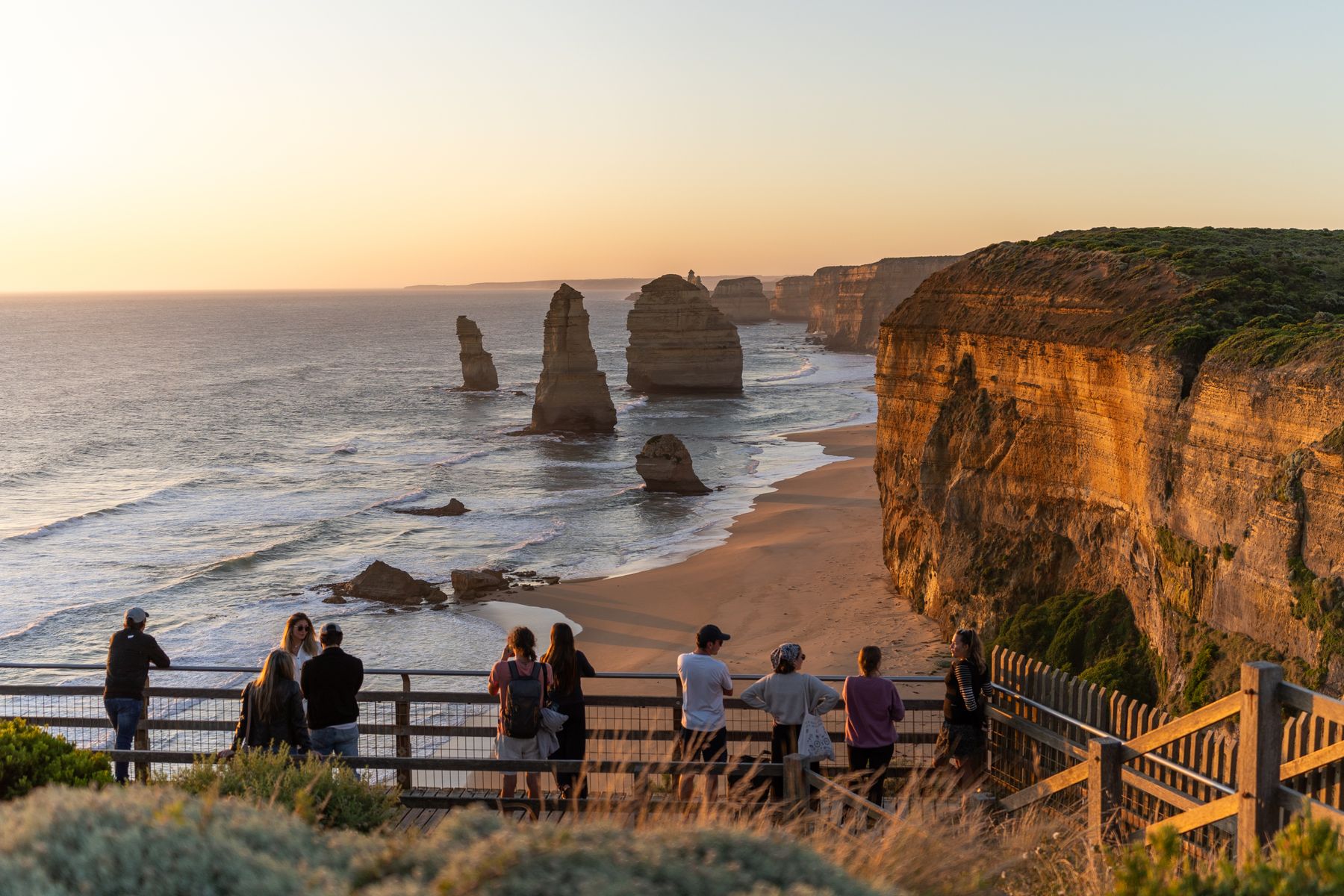 Travelers overlooking the Twelve Apostles rock stacks on Victoria's Great Ocean Road at sunset