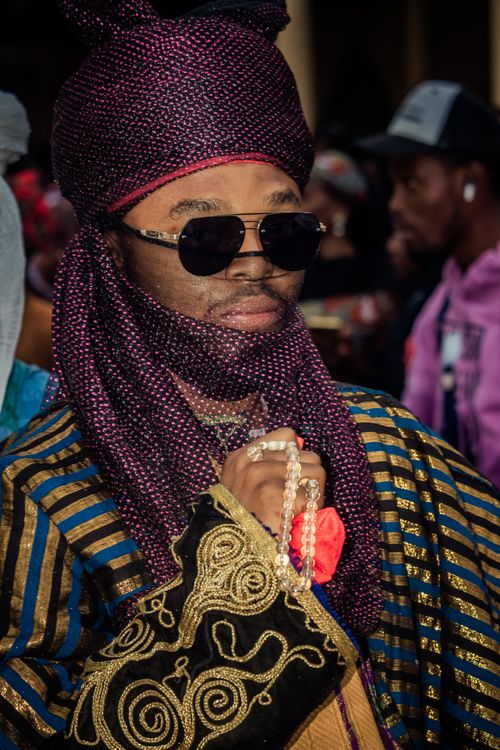 Free Man in vibrant traditional Nigerian attire with intricate patterns, wearing sunglasses at a cultural event. Stock Photo