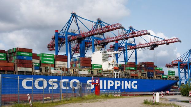 Large container ship docked at Hamburg port with towering cranes and shipping containers.