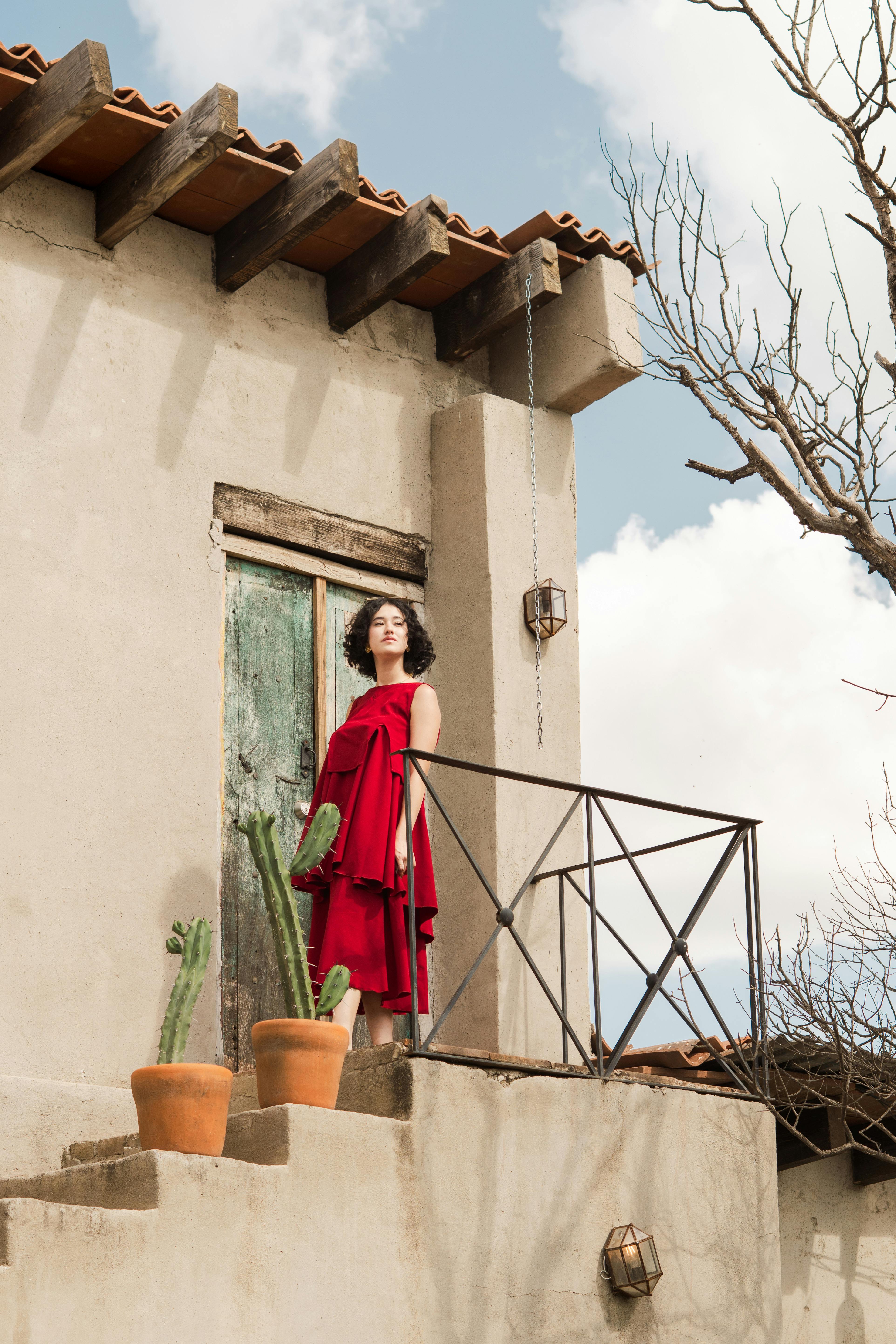 A stylish woman in a red dress stands on a rustic balcony in Santiago de Querétaro.