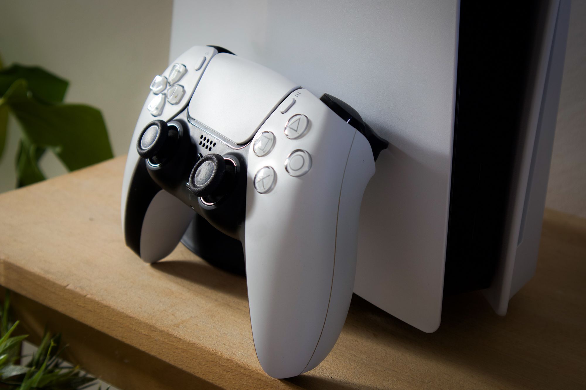 Close-up of PlayStation 5 with DualSense controller on a wooden shelf.