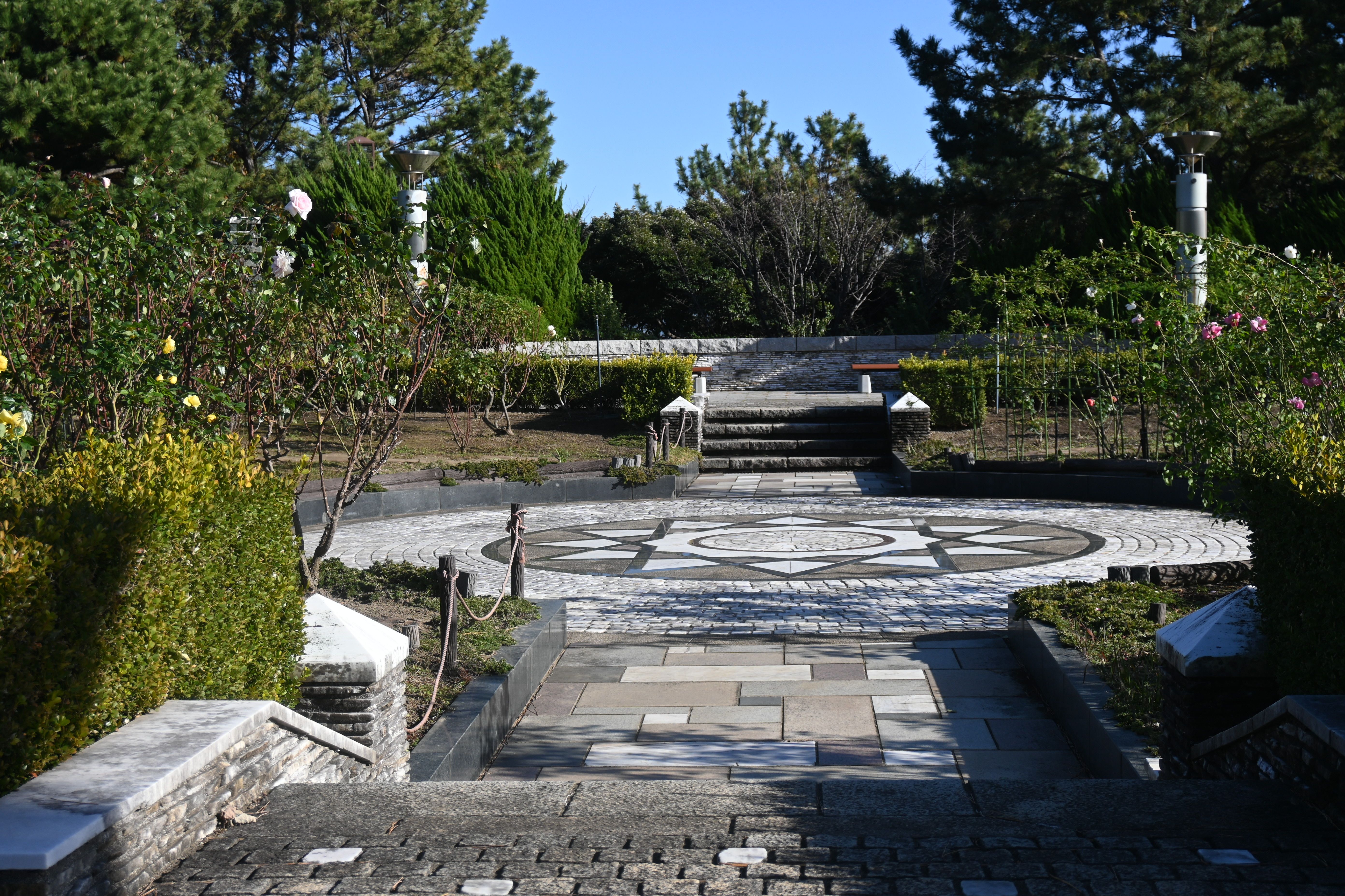 A serene stone pathway leads to a garden surrounded by lush greenery and geometric paving design.