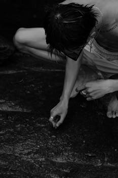 Moody black and white image of a person closely examining the ground surface.