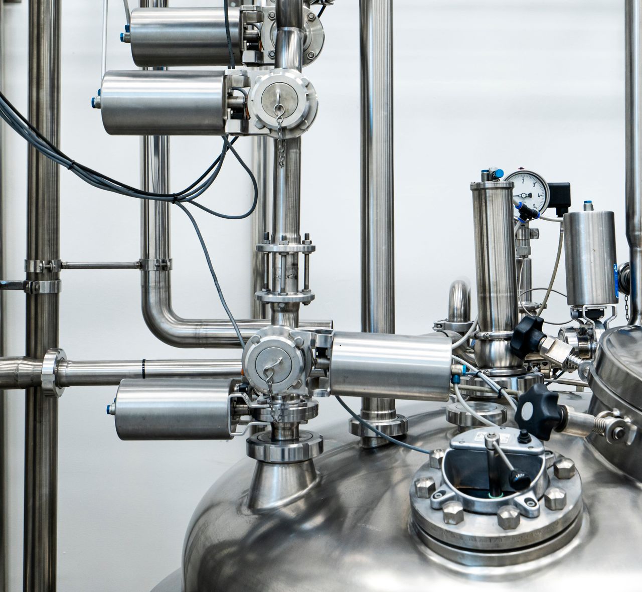Close-up of stainless steel process pipework, clamped fittings and a vessel head fitted with instrumentation.