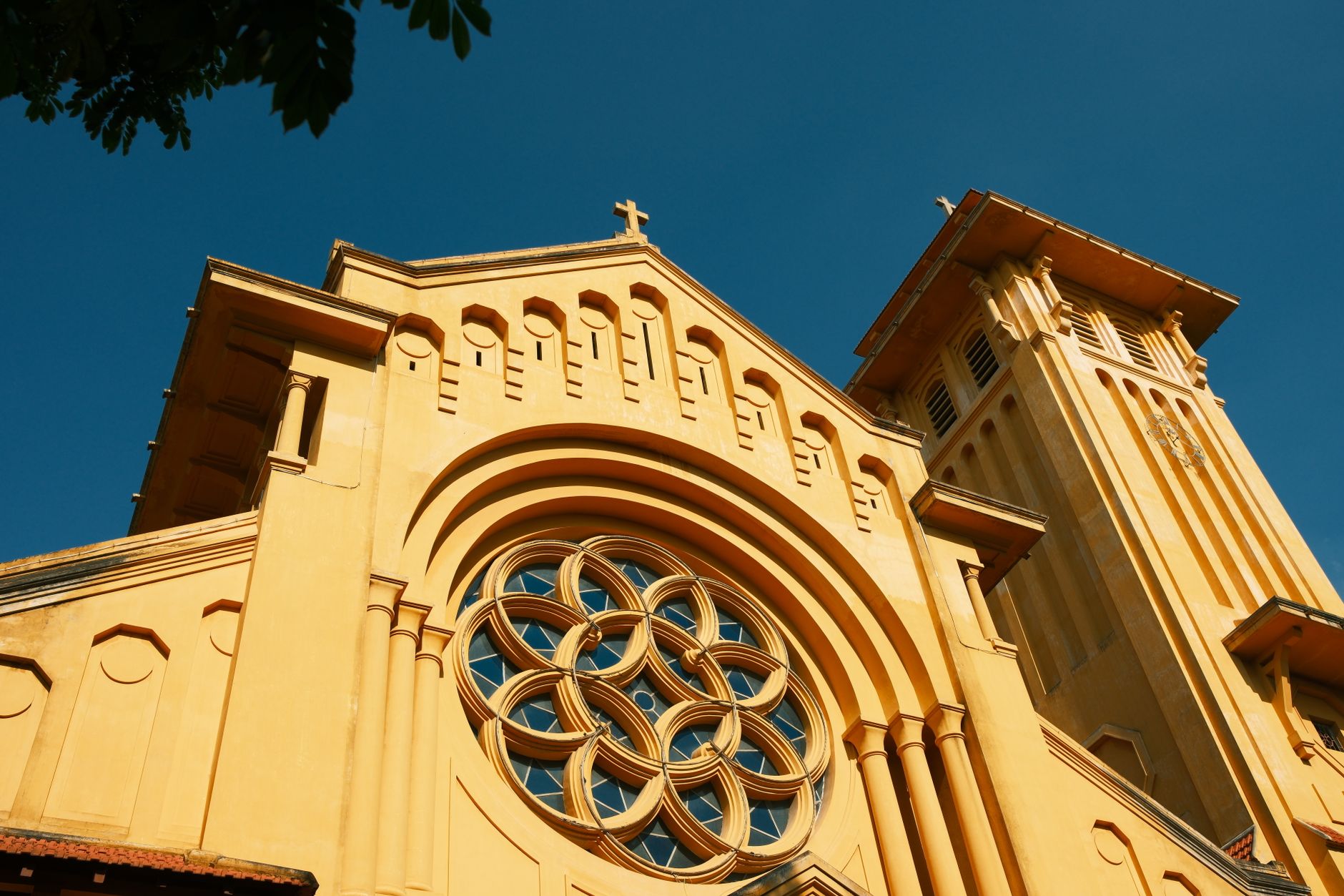 Striking image of a yellow Catholic church facade against blue sky in Hanoi, Vietnam.