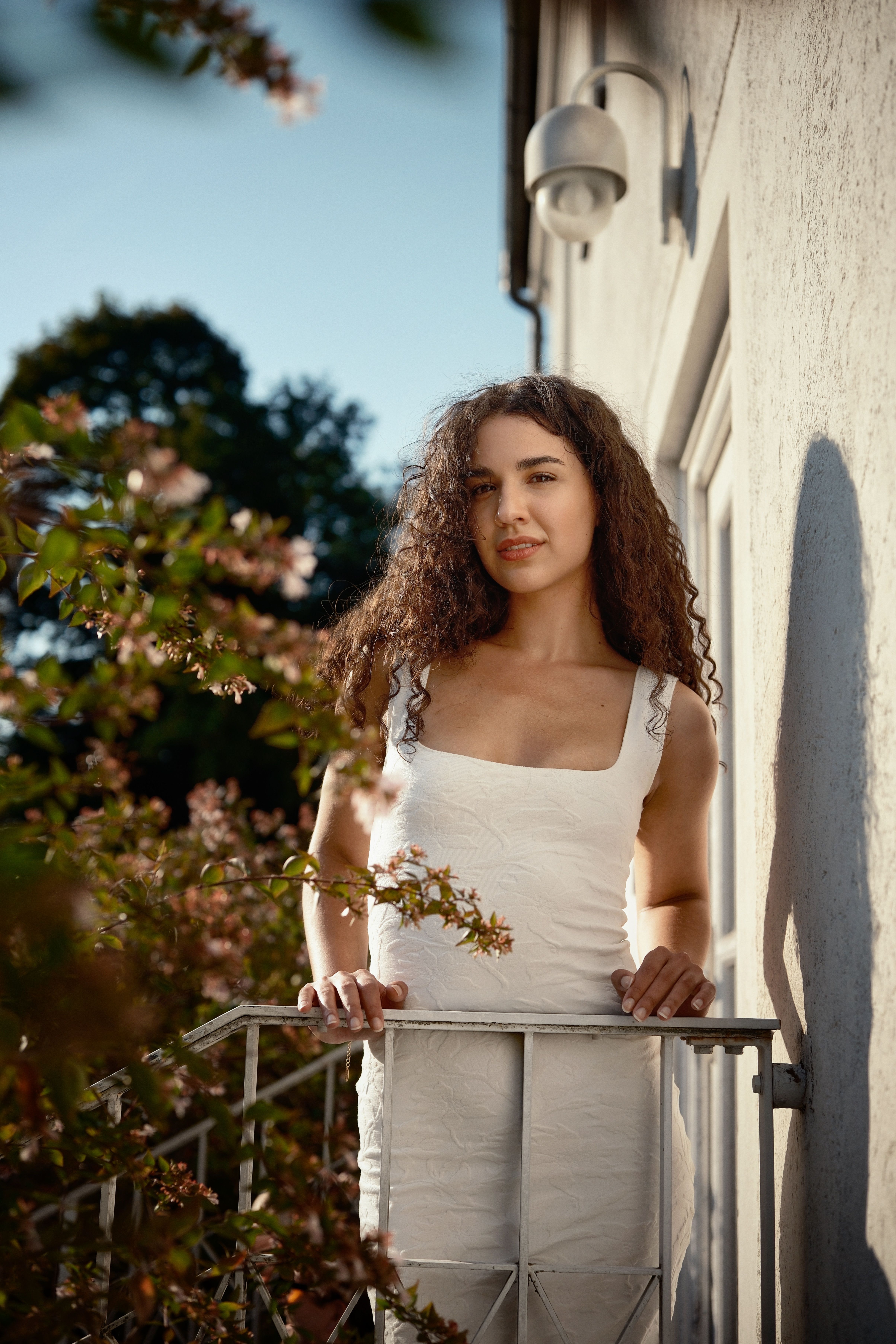 Portrait of a young woman in a white dress on a balcony with flowers.