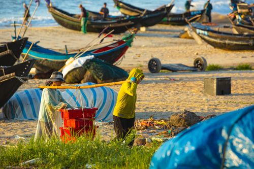 Free Fishermen transporting baskets on a sandy beach near traditional boats under the sun. Stock Photo