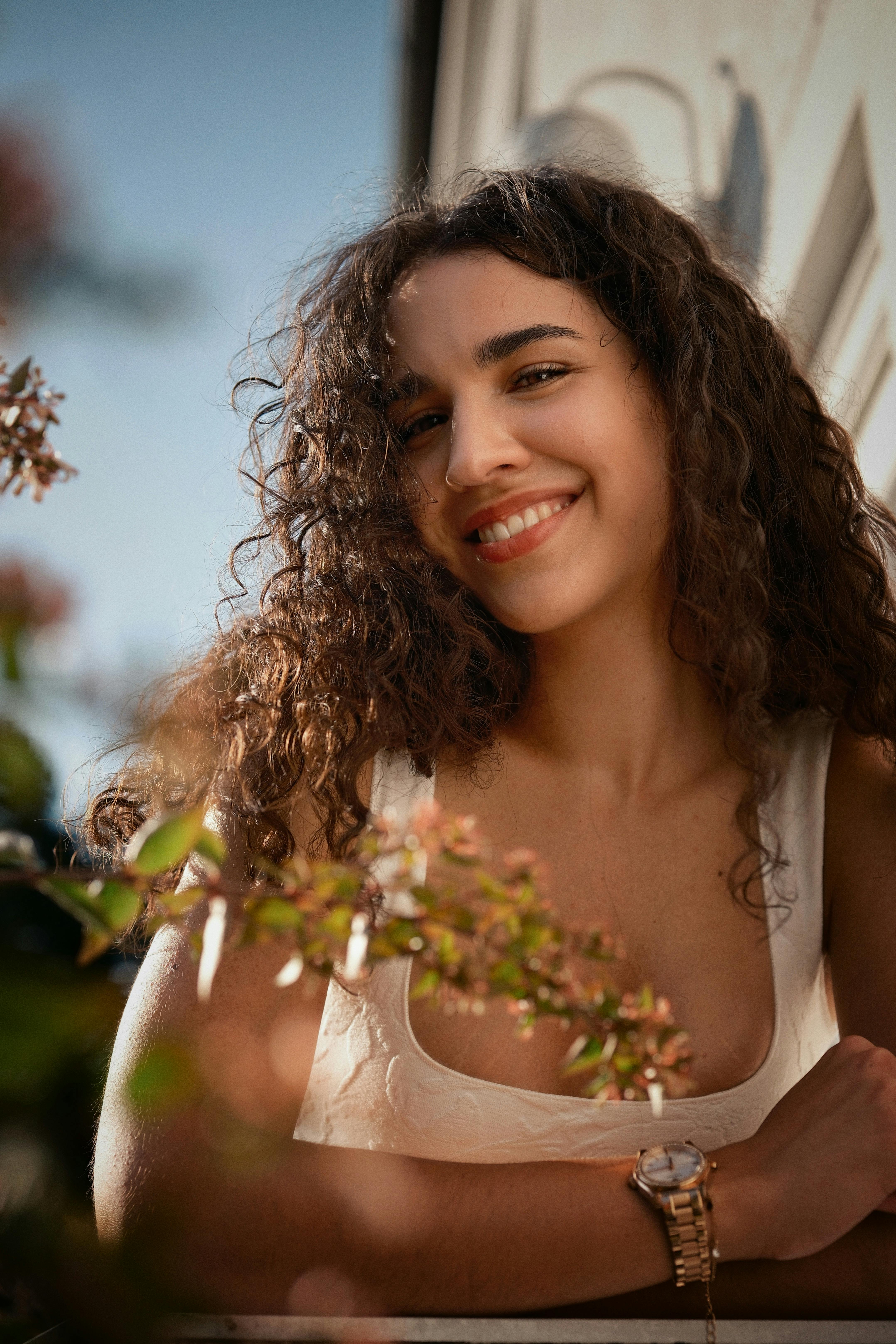 A joyful woman with curly hair smiling outdoors, creating a warm and vibrant mood.