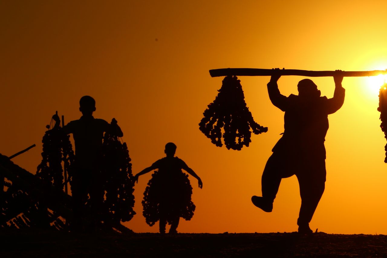 silhouetted people carrying bundles against a vibrant sunset backdrop