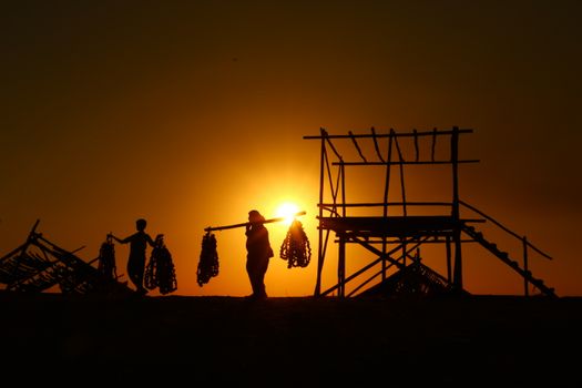 Silhouette of fishermen carrying nets against a stunning sunset backdrop.