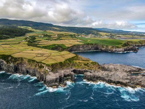 Free A breathtaking aerial view of coastal cliffs and lush farmlands under a cloudy sky. Stock Photo