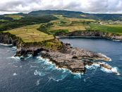 Stunning aerial view of rocky cliffs and lush fields meeting the ocean in a coastal landscape.