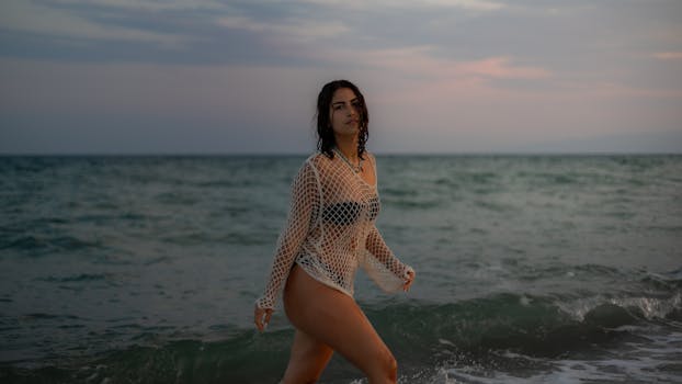 A woman in a fishnet top walks along the beach in Calabria, Italy at sunset.