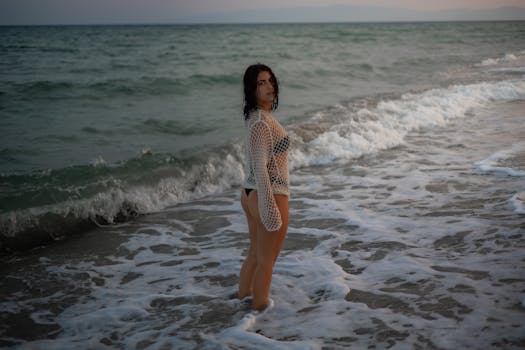 Serene beach portrait of a woman standing in the waves at sunset in Calabria, Italy.