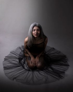 Elegant portrait of a woman kneeling in a dark tulle skirt, exuding grace and serenity.