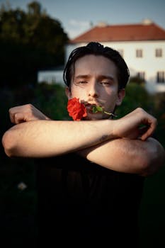 A moody portrait of a man holding a rose in an outdoor setting with soft evening light.