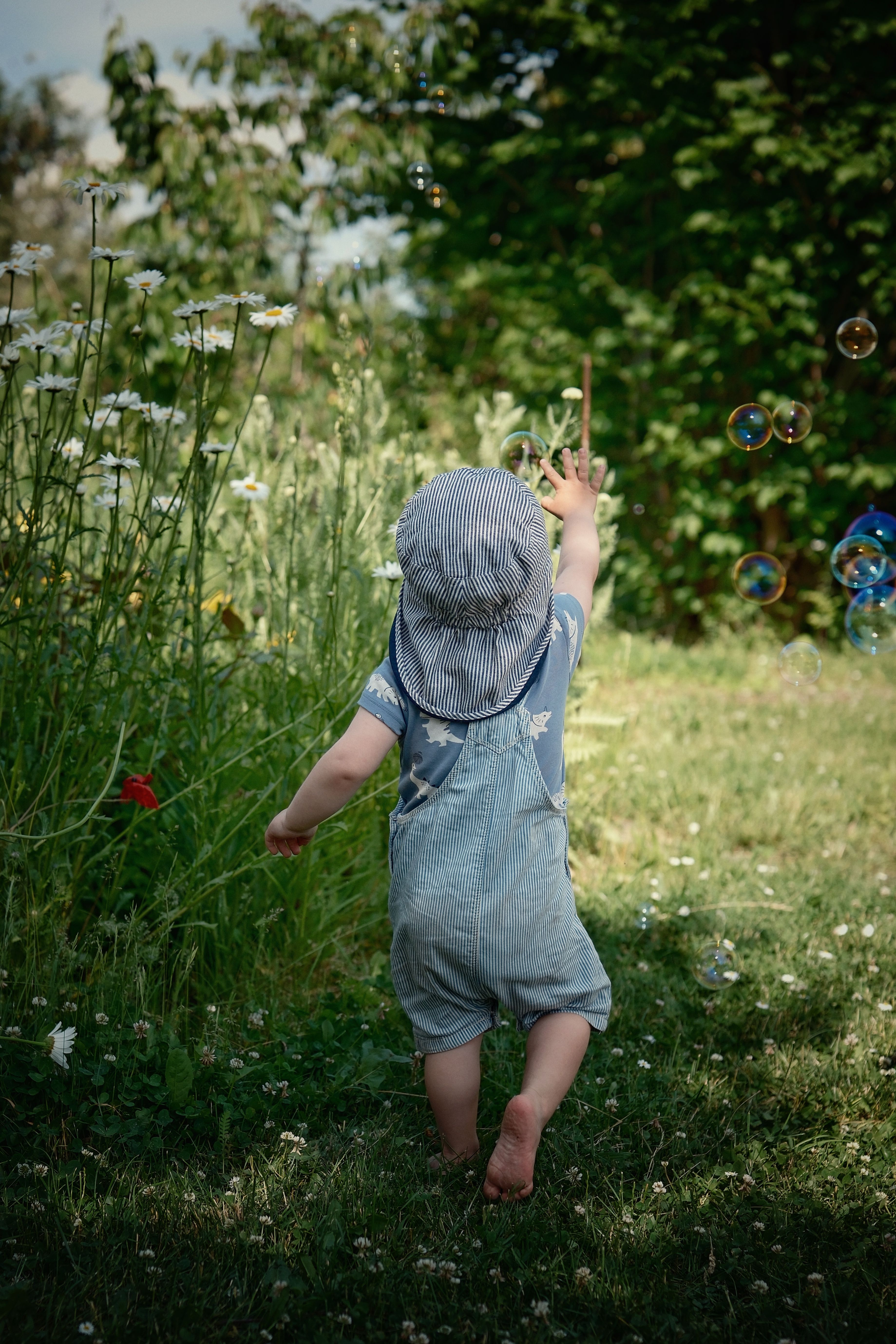 A cute toddler enjoys a sunny day outdoors, chasing bubbles in a lush garden.
