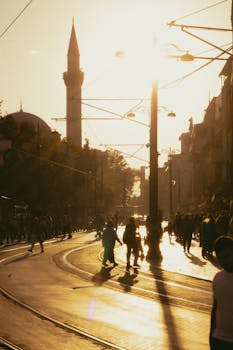 Silhouetted people walking near Istanbul tram line at sunset with city skyline.