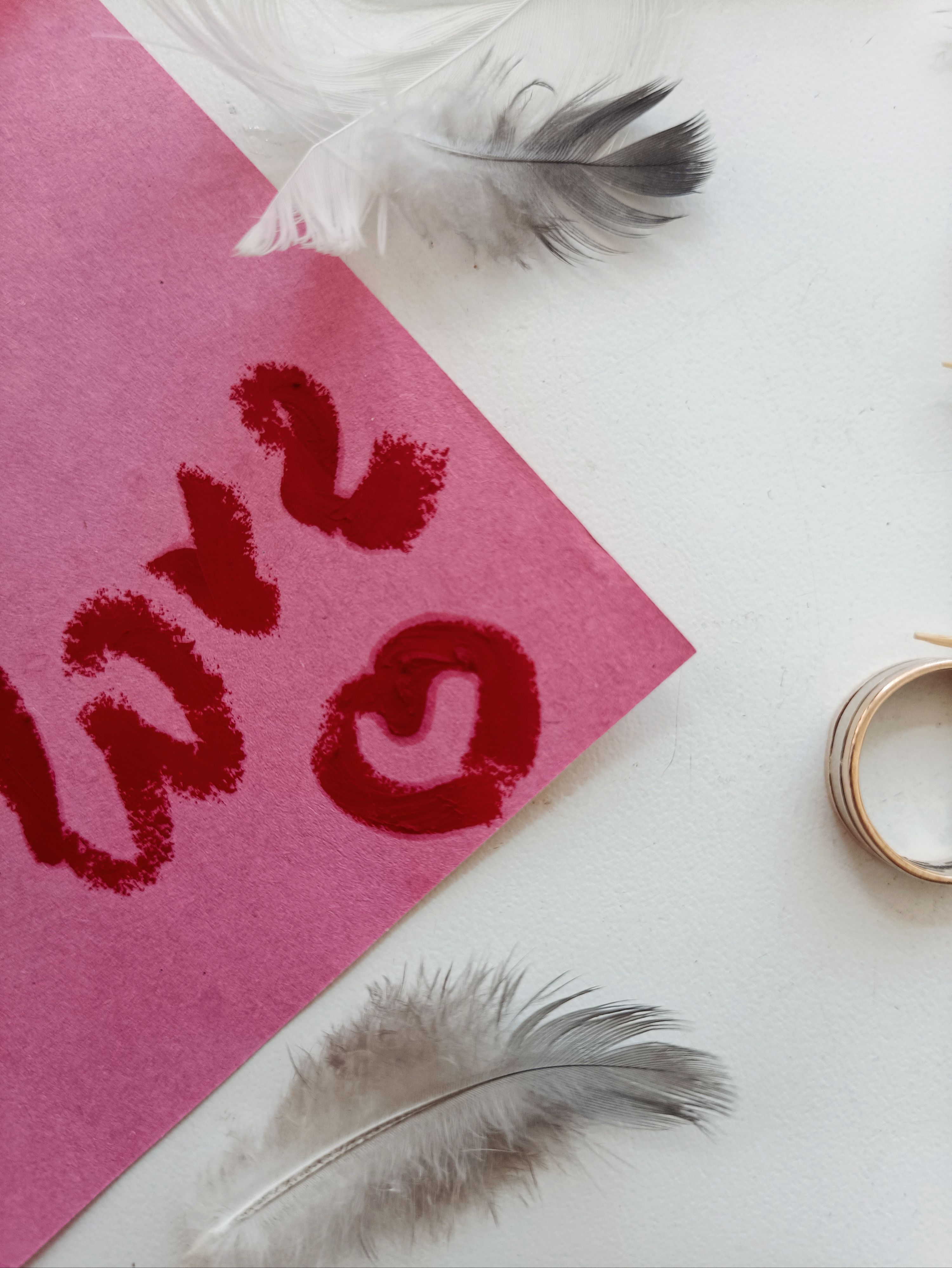 Artistic flat lay of a love note, feathers, and rings on a white surface.