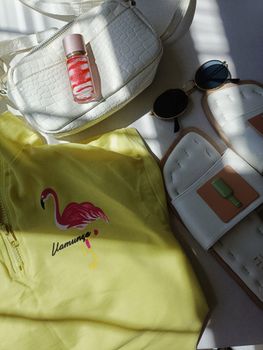 Flat lay of summer fashion accessories including a yellow flamingo shirt, white bag, and sunglasses.