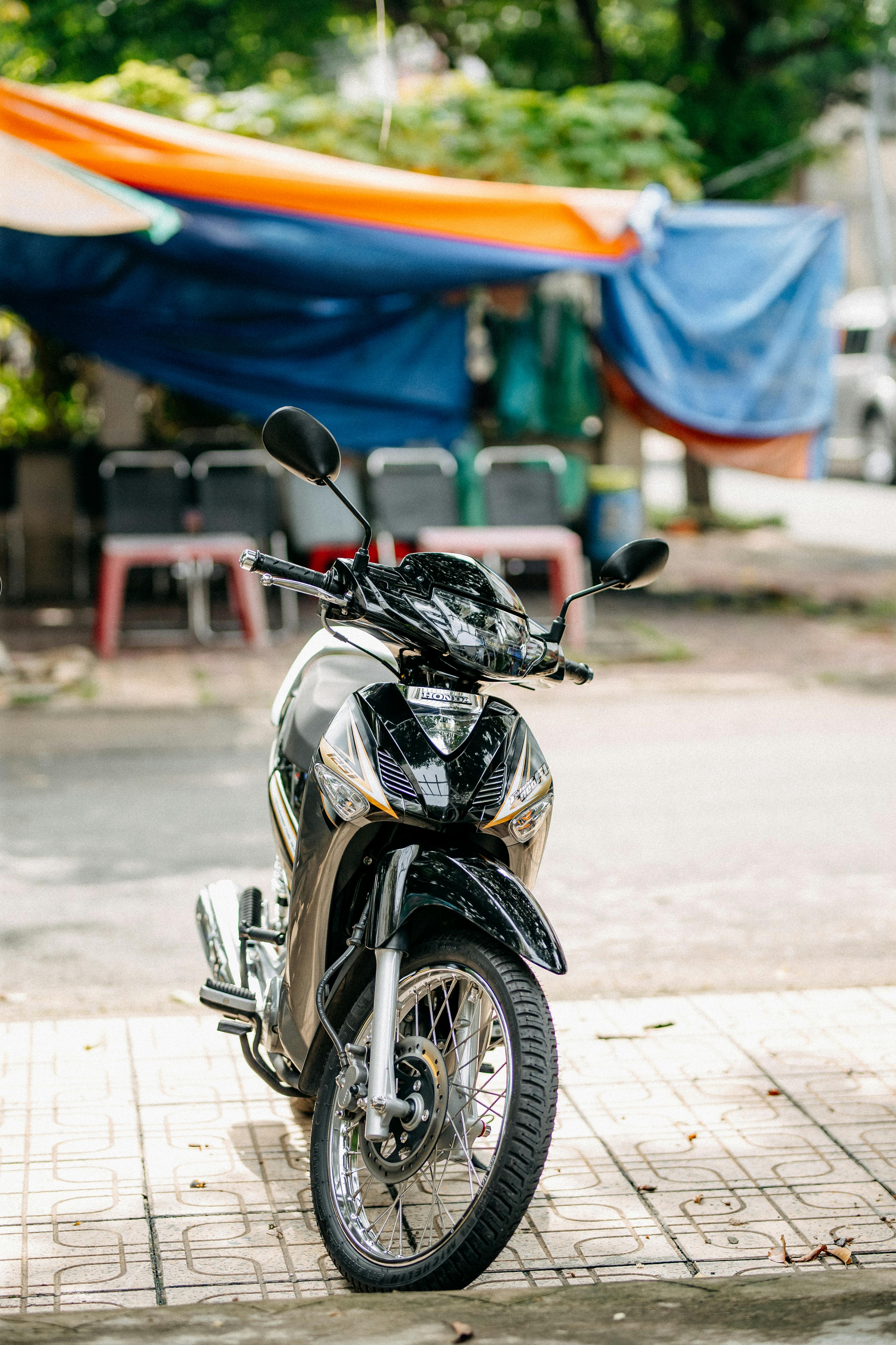 Free A sleek black motorcycle parked on a tiled pavement, with colorful fabric canopy in background. Stock Photo