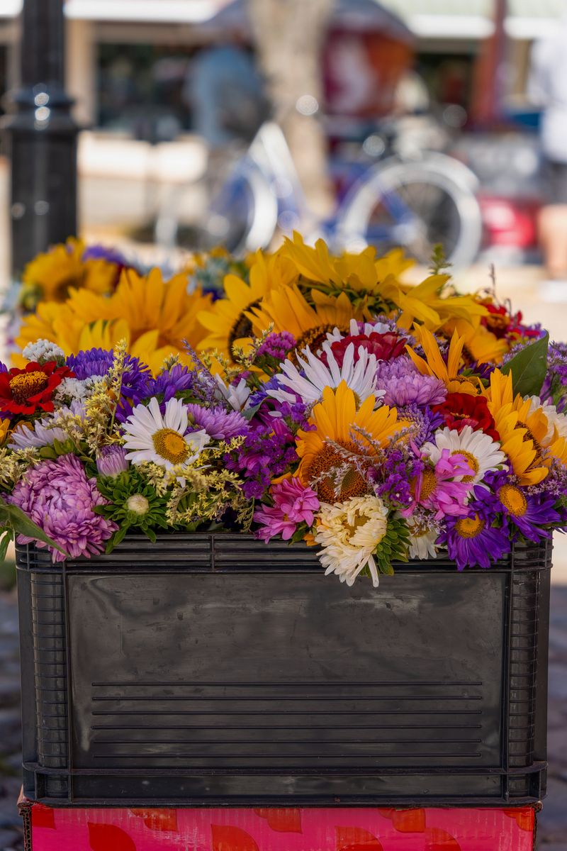 Colorful assortment of summer flowers including sunflowers in an outdoor market setting.