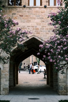 Picturesque view through archway framed by blooming trees, stone walls enhance historic charm.