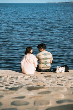 A couple enjoying a peaceful moment sitting by the sea with clear blue waters and sunny skies.