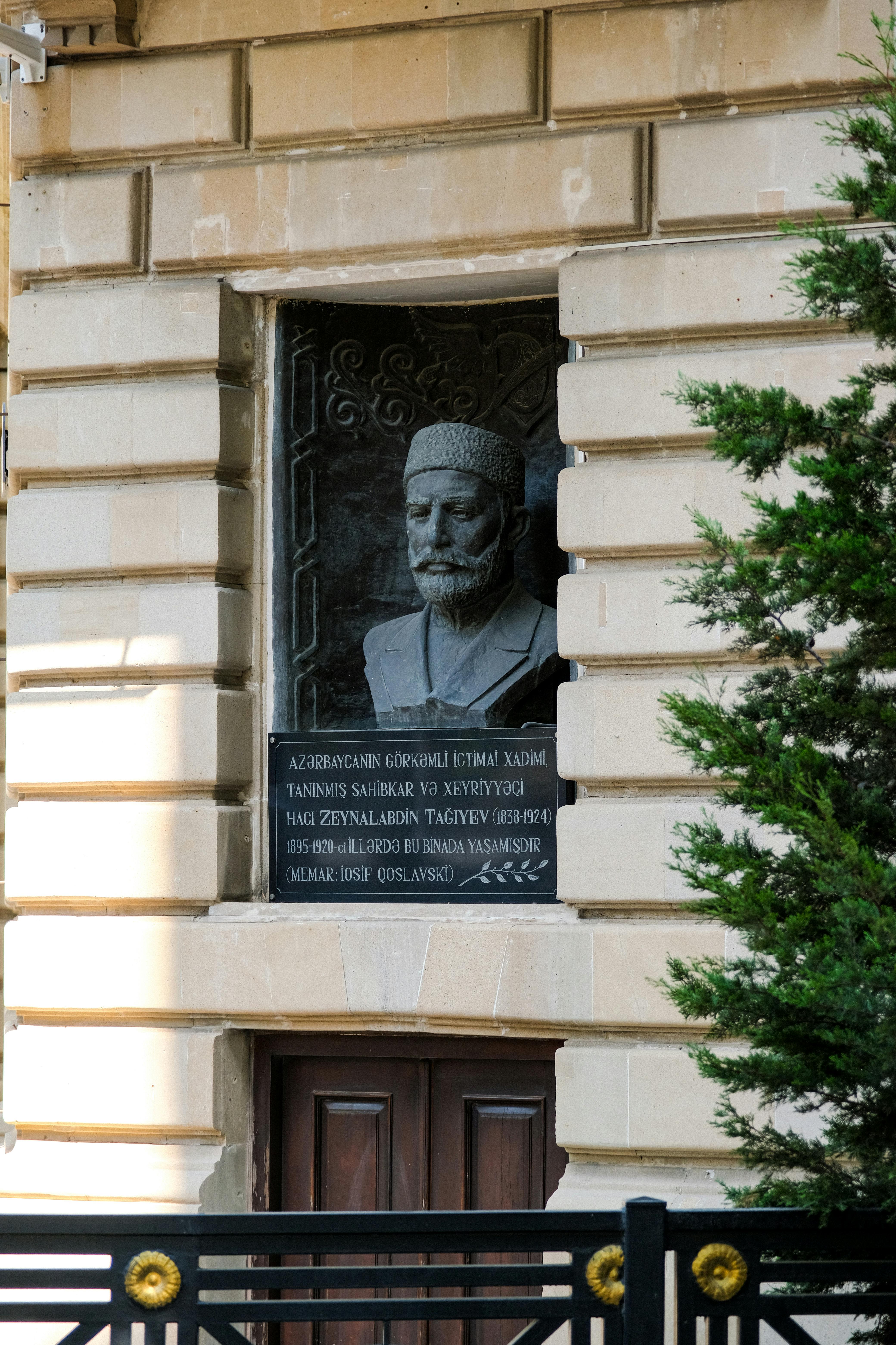 A commemorative plaque with a bust, set in an urban wall, captured in daylight.