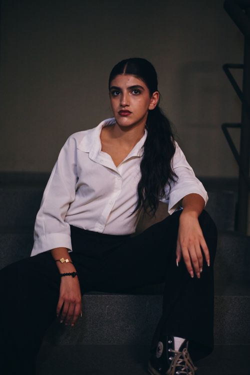 Free Stylish portrait of a woman in a white shirt and dark pants sitting on stairs, showcasing urban fashion. Stock Photo