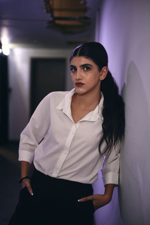 Free Confident woman in a white shirt leaning against a wall with a modern, editorial look. Stock Photo