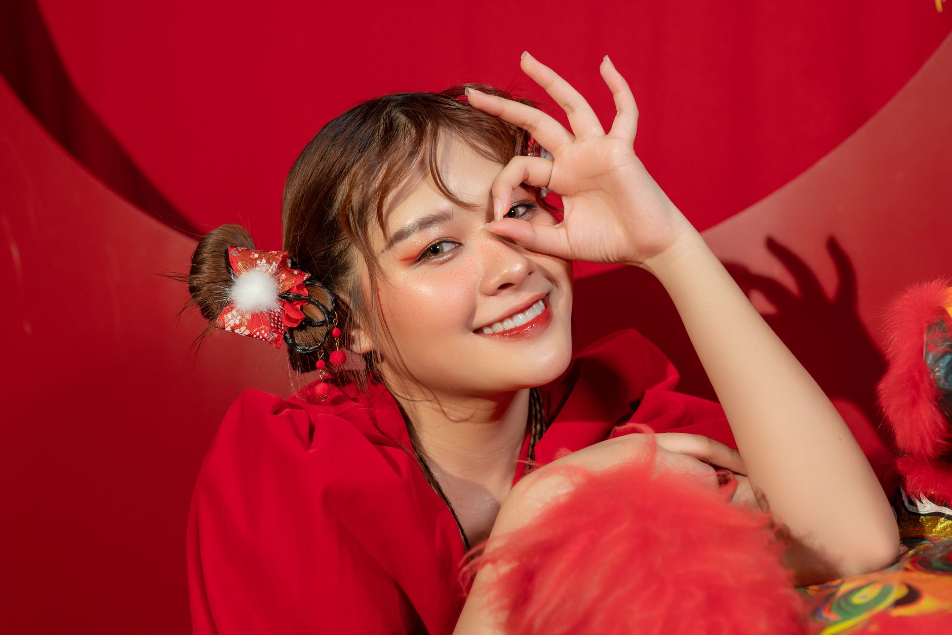 Smiling woman making eye gesture, adorned in red, exuding a festive and joyful mood.