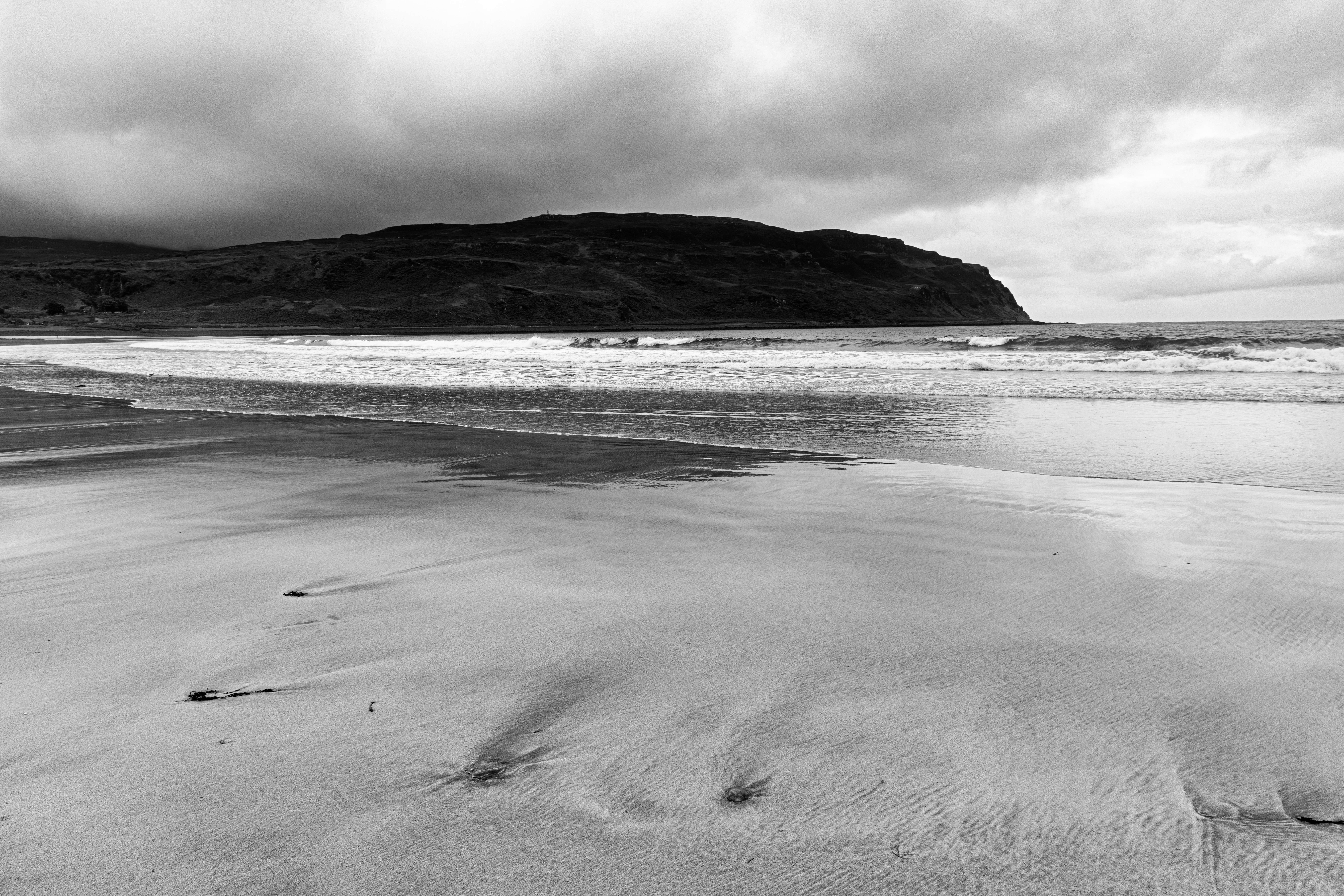 Moody black and white image of a Scottish beach with waves and dramatic clouds.