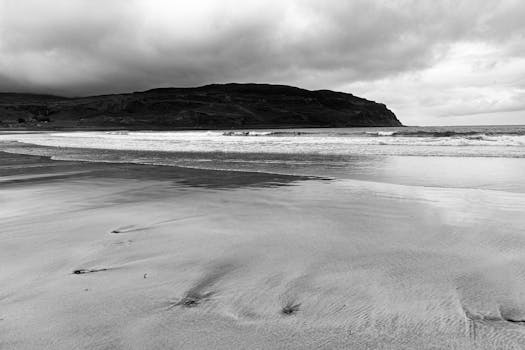 Moody black and white image of a Scottish beach with waves and dramatic clouds.