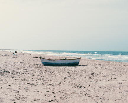 An abandoned boat rests on a quiet, sandy beach under a clear sky.