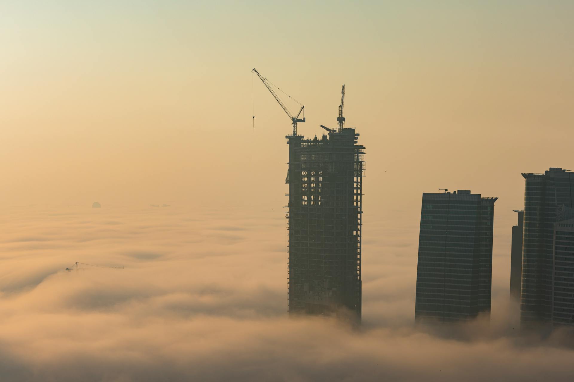 Aerial view of Dubai skyscrapers emerging from thick fog during construction at dawn.