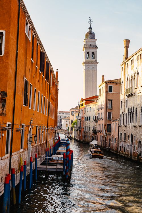 Free A picturesque canal in Venice, Italy with historic buildings and a leaning bell tower at sunset. Stock Photo