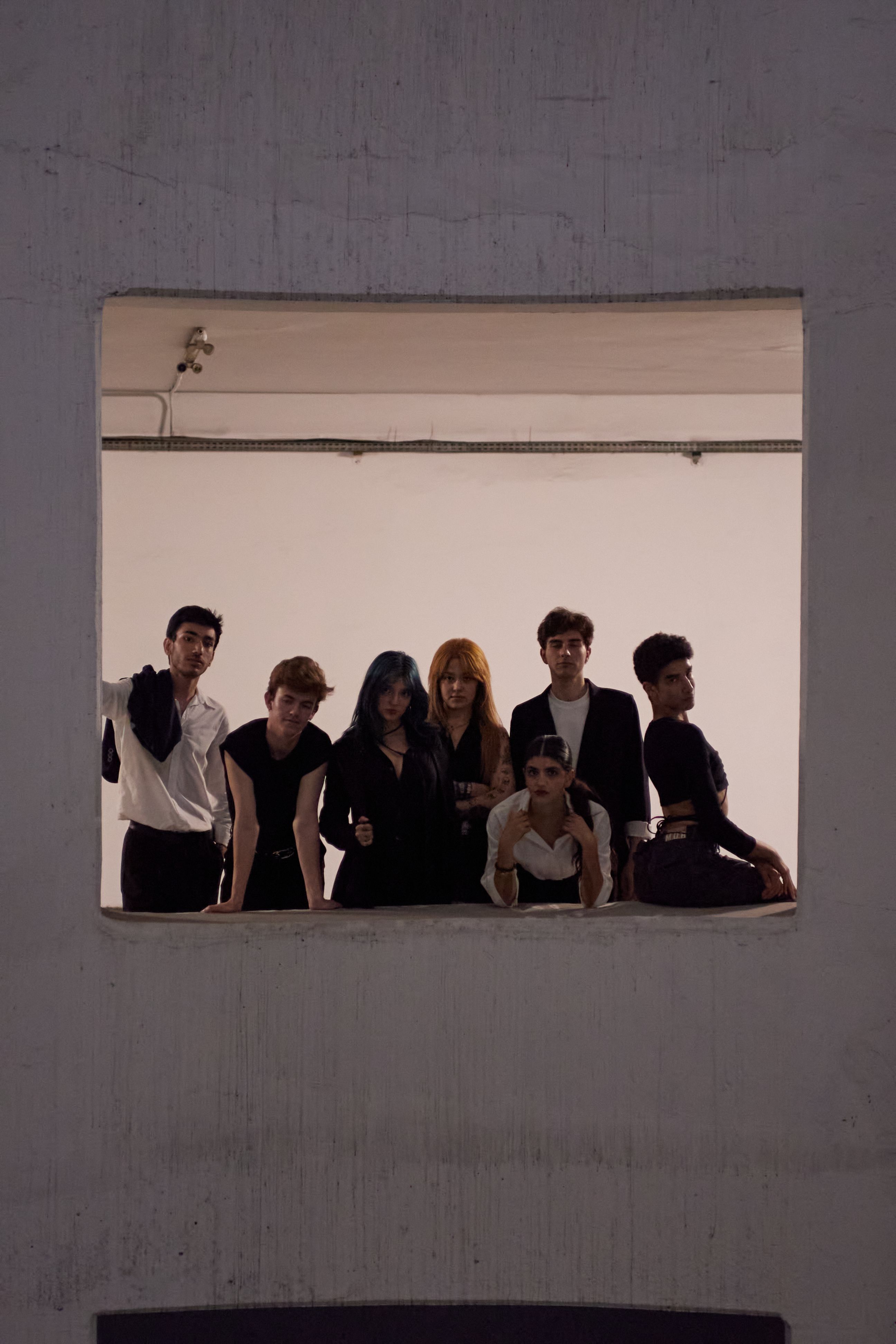 Group of young adults in stylish outfits posing indoors through a window.