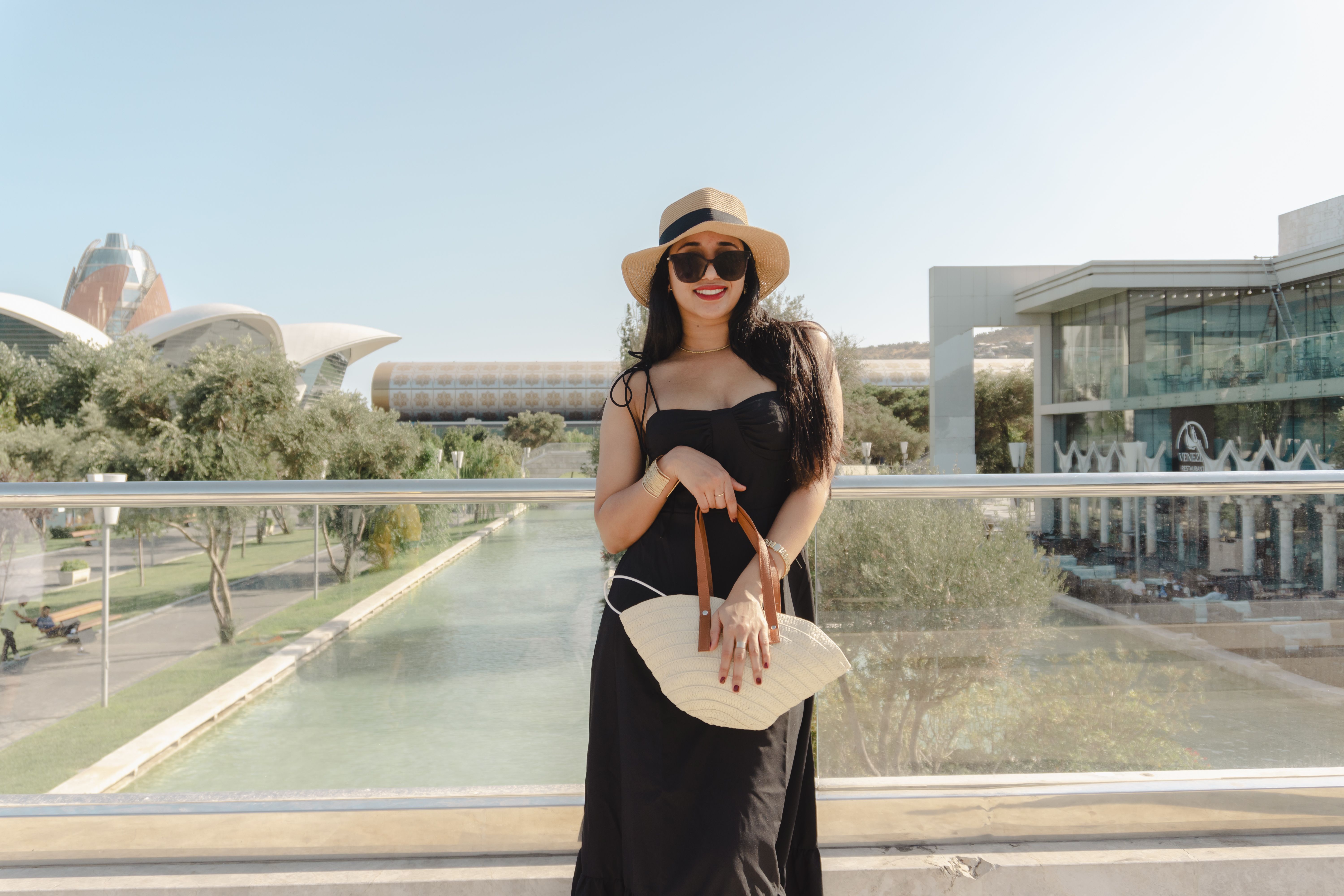A fashionable woman with a hat poses by the waterway in Baku, Azerbaijan, on a sunny day.