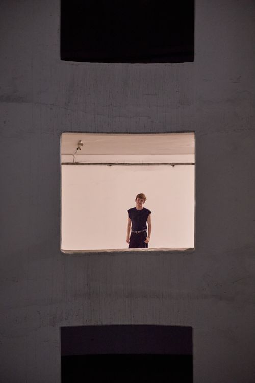 Free Striking portrait of a young woman framed in a modern urban window, presenting a unique fashion editorial style. Stock Photo