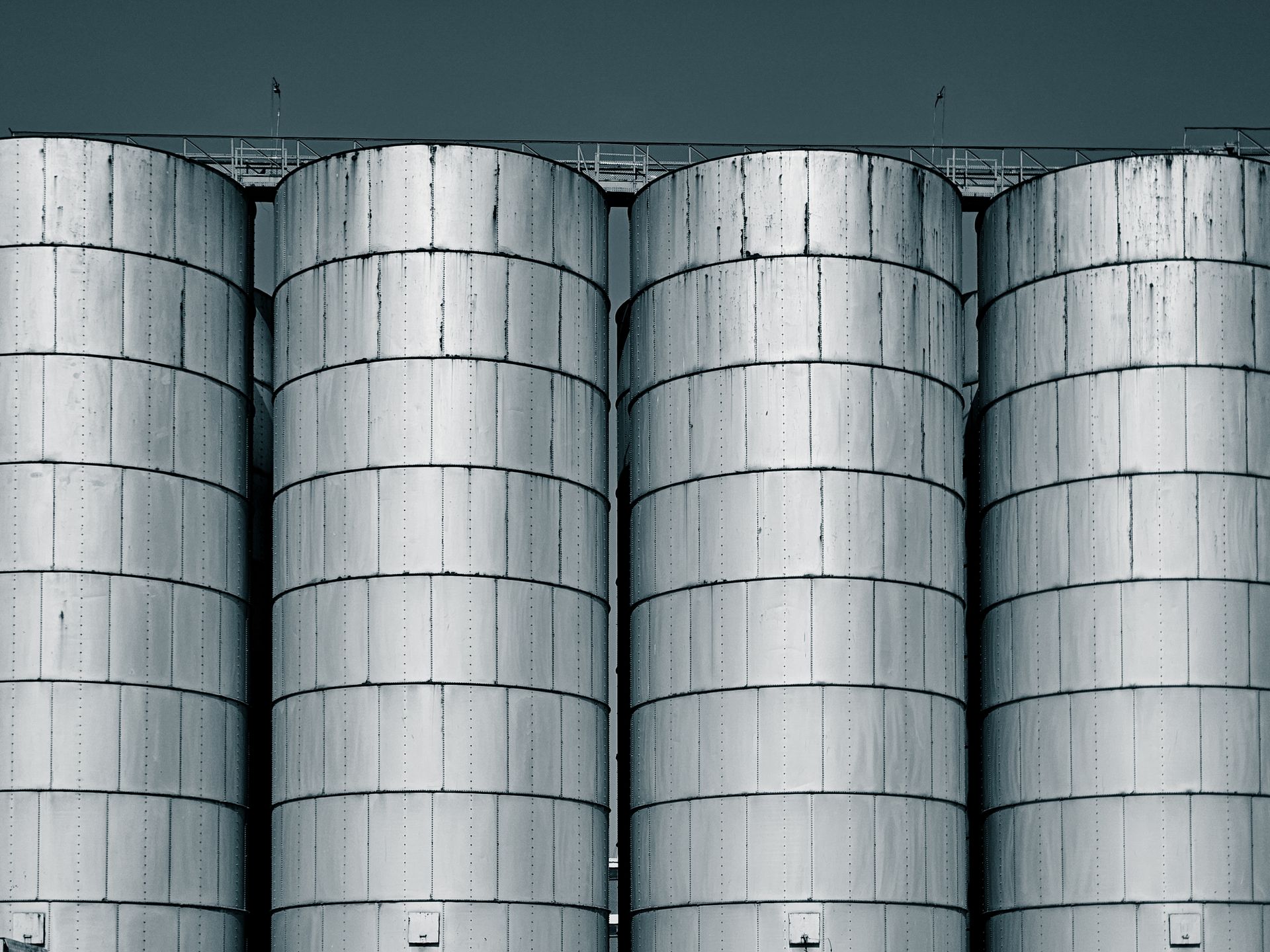 Four large industrial steel silos with a cool-toned sky backdrop.