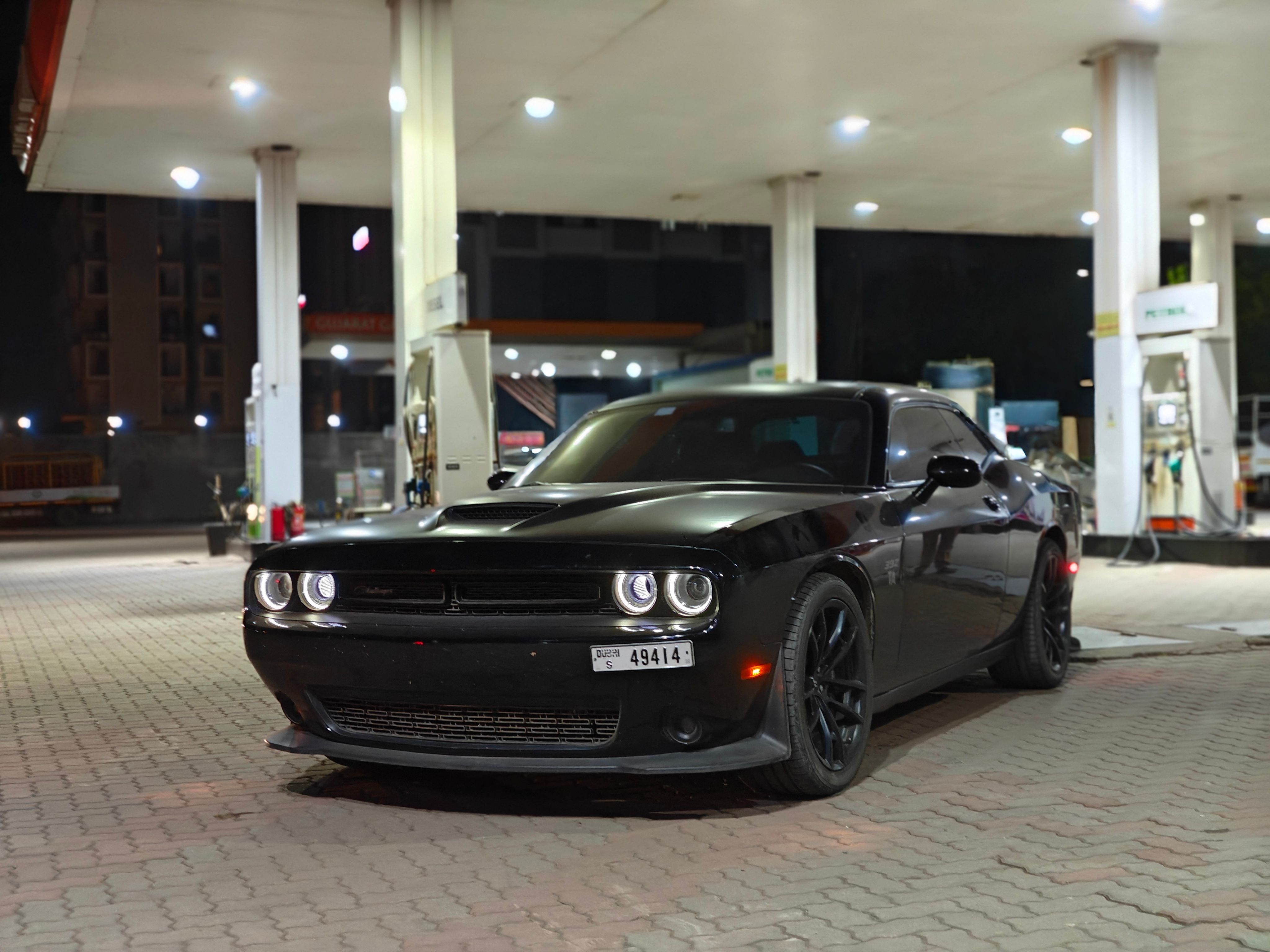 Black car parked at a gas station under bright lights during nighttime.