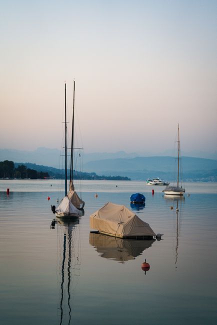 Peaceful lake scene at dawn with sailboats and calm waters, perfect for relaxation and travel themes.