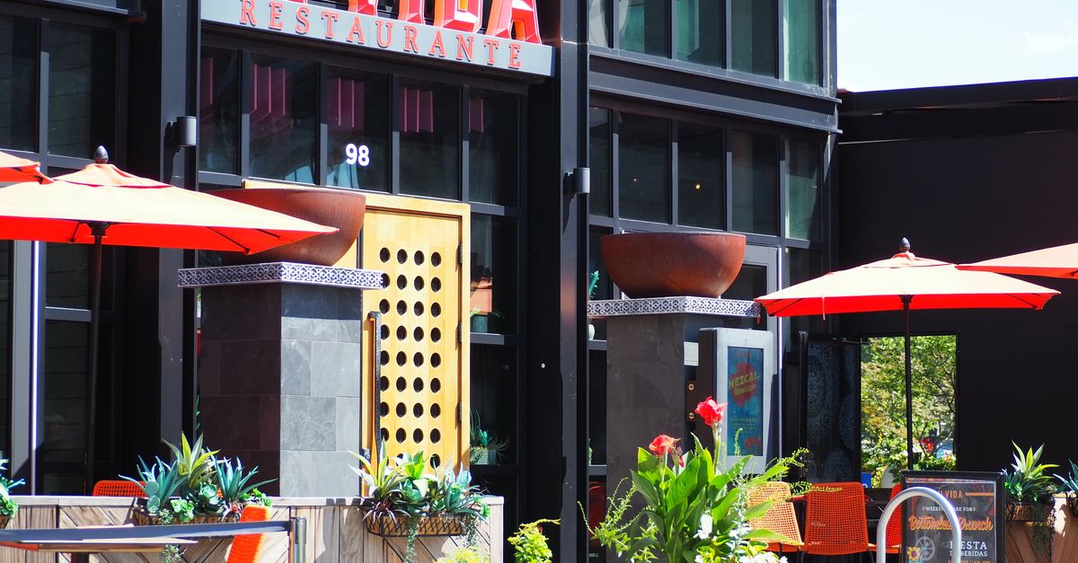 Colorful outdoor seating at Mi Vida Restaurant in Washington, DC, with red umbrellas and lush plants.